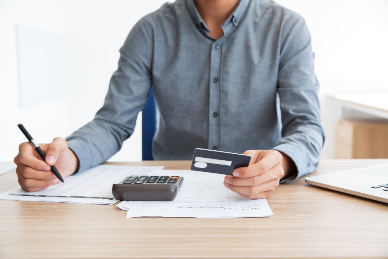 Close-up of unrecognizable man writing credit card number and planning his budget. Or businessman calculating company income in office. Paperwork or finance concept